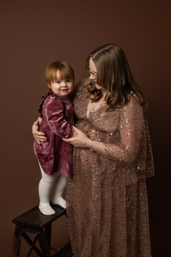 Gravid med glittrig lyxig klänning tillsammans med sin dotter.