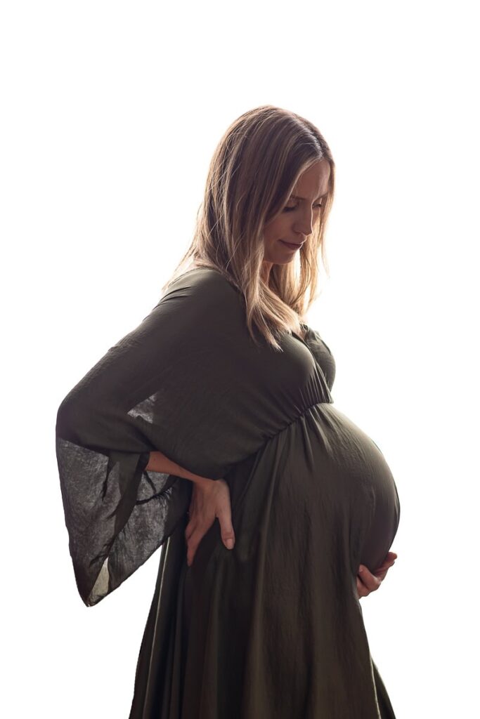 Gravid i motljus i en grön vacker gravidklänning