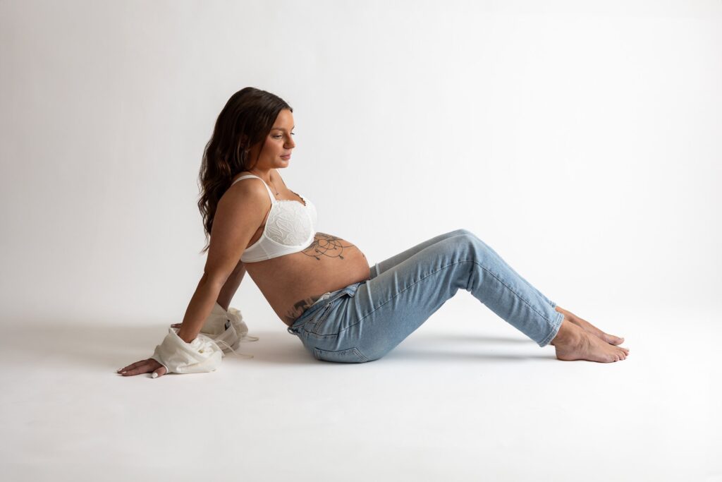 Gravid sittande på golvet i jeans och nerhasad skjorta.